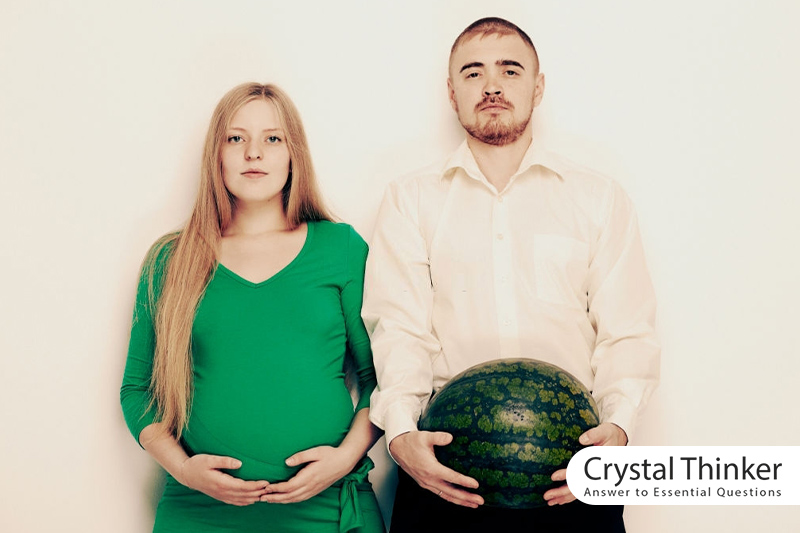 A man with a watermelon in his hand next to his pregnant wife
