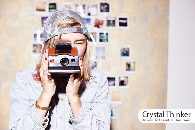 Young woman in front of a photo wall and taking pictures with a nostalgic camera